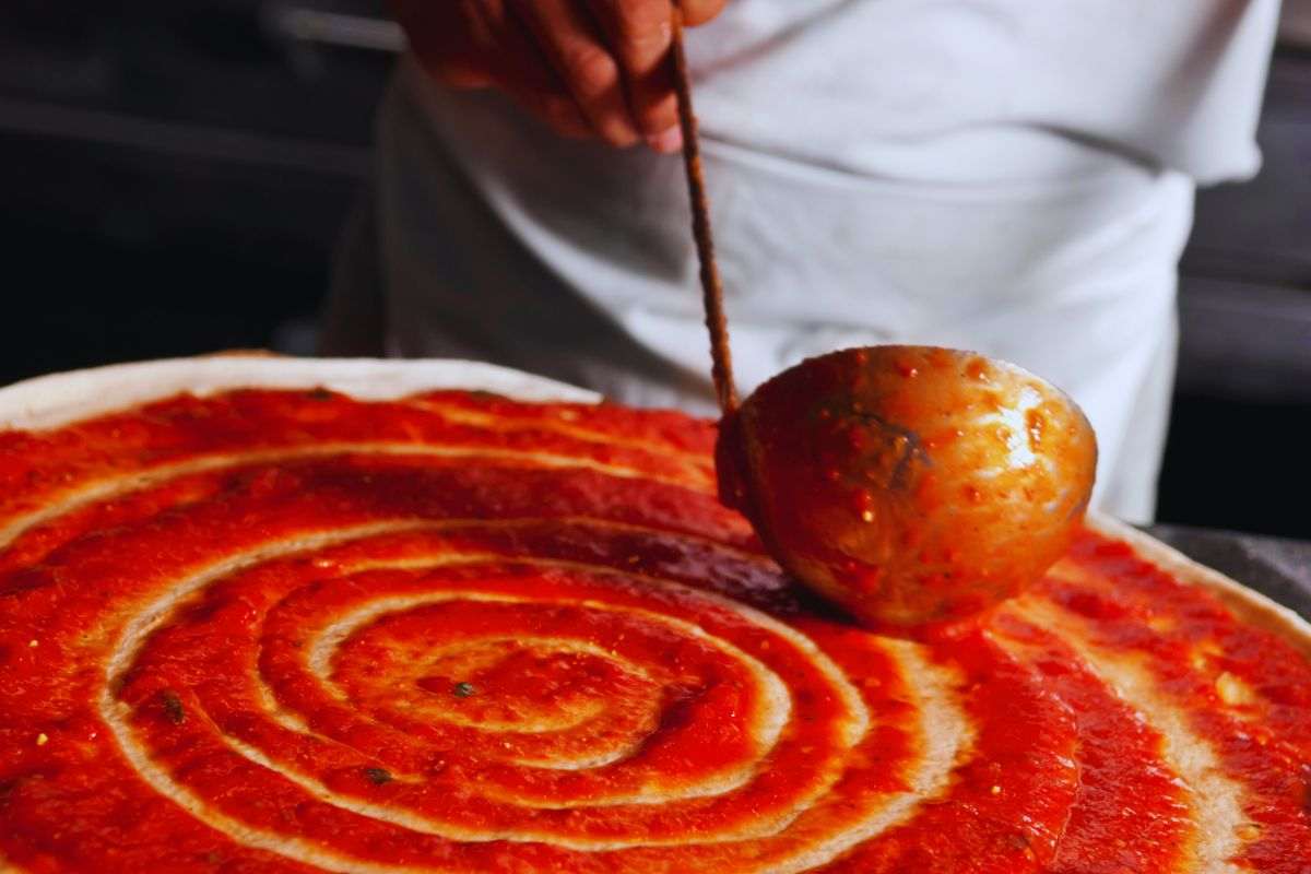 pizzaiolo mette sugo sulla pizza