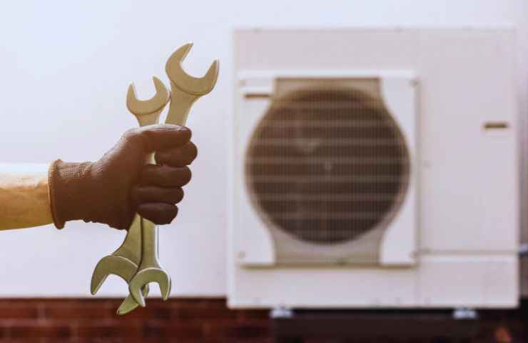 il motore di una pompa di calore e una mano con due chiavi inglesi