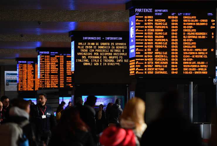 persone in stazione di fronte ai tabelloni dei treni