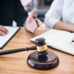 Martelletto di un giudice sulla scrivania mentre due avvocati sullo sfondo lavorano a una causa