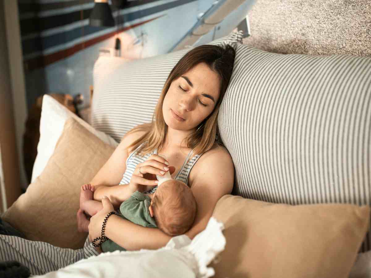 Una mamma stesa su un letto che dà il latte al figlio neonata