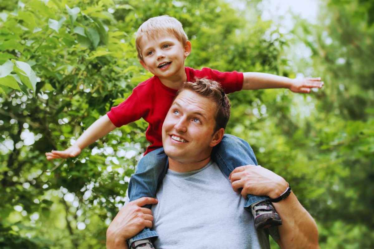 un bambino fa l'aeroplano sulle spalle del padre