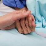 Una figlia stringe la mano alla madre anziana in fin di vita