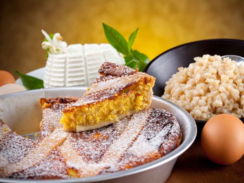Pastiera napoletana con accanto gli ingredienti principali per preparare il dolce di Pasqua