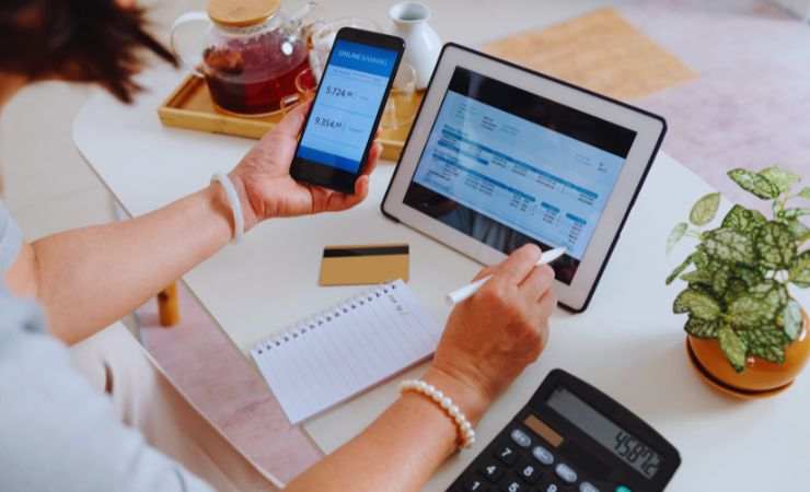 una ragazza fa i conti con fogli, penna, tablet e smartphone