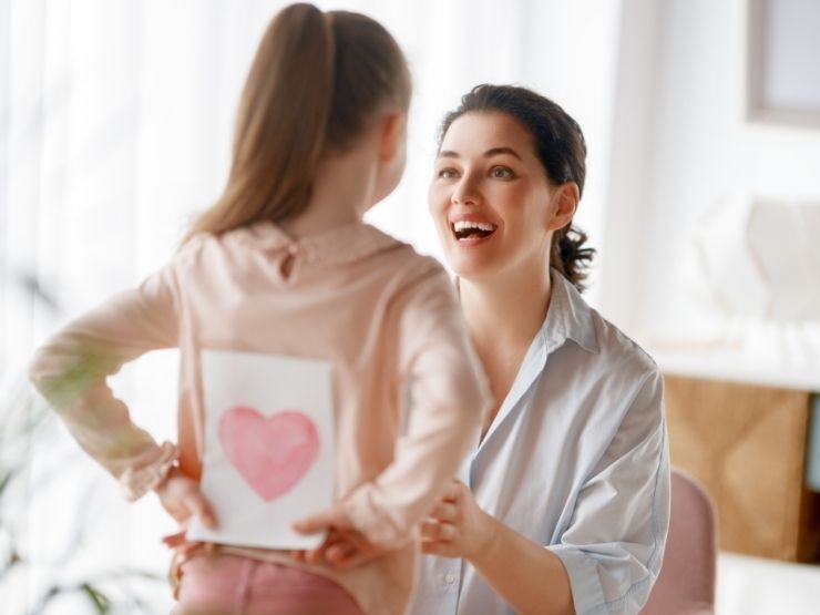 Una bimba regala un disegno raffigurante un cuore alla madre. La madre è felice