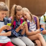 Bambini seduti su un muretto fuori dalla scuola mentre usano lo smartphone