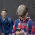 Un bambino con il cellulare viene preso in giro dai compagni di scuola