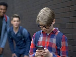 Un bambino con il cellulare viene preso in giro dai compagni di scuola