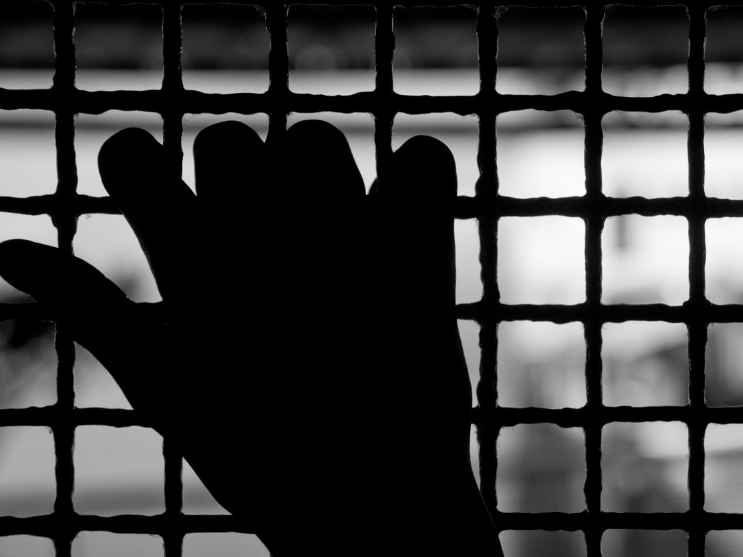 Mano che stringe una grata di una cella, la drammatica condizione delle carceri italiane