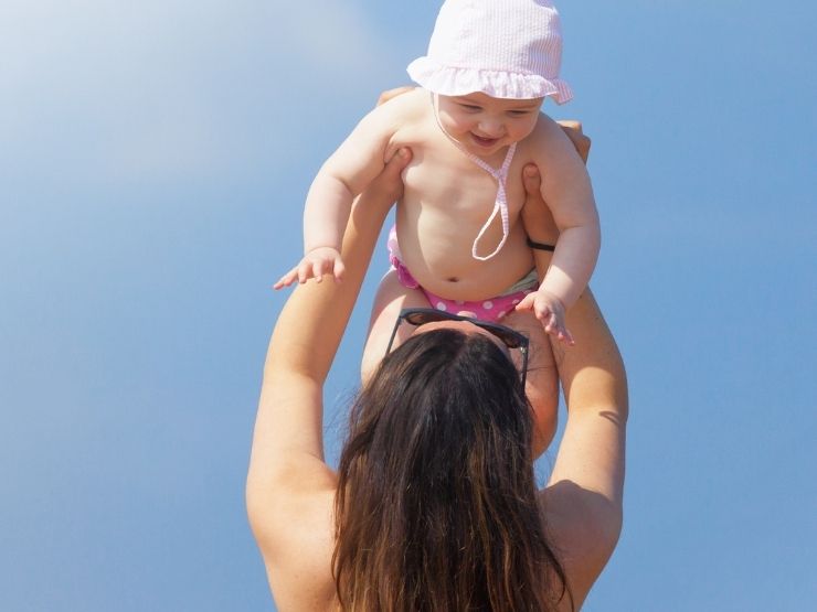 Una neonata sorride felice mentre gioca con la madre in spiaggia
