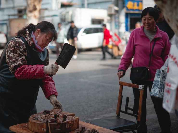 Una donna taglia del pesce in strada a Wuhan, in Cina, dove sarebbe partita la pandemia da Covid