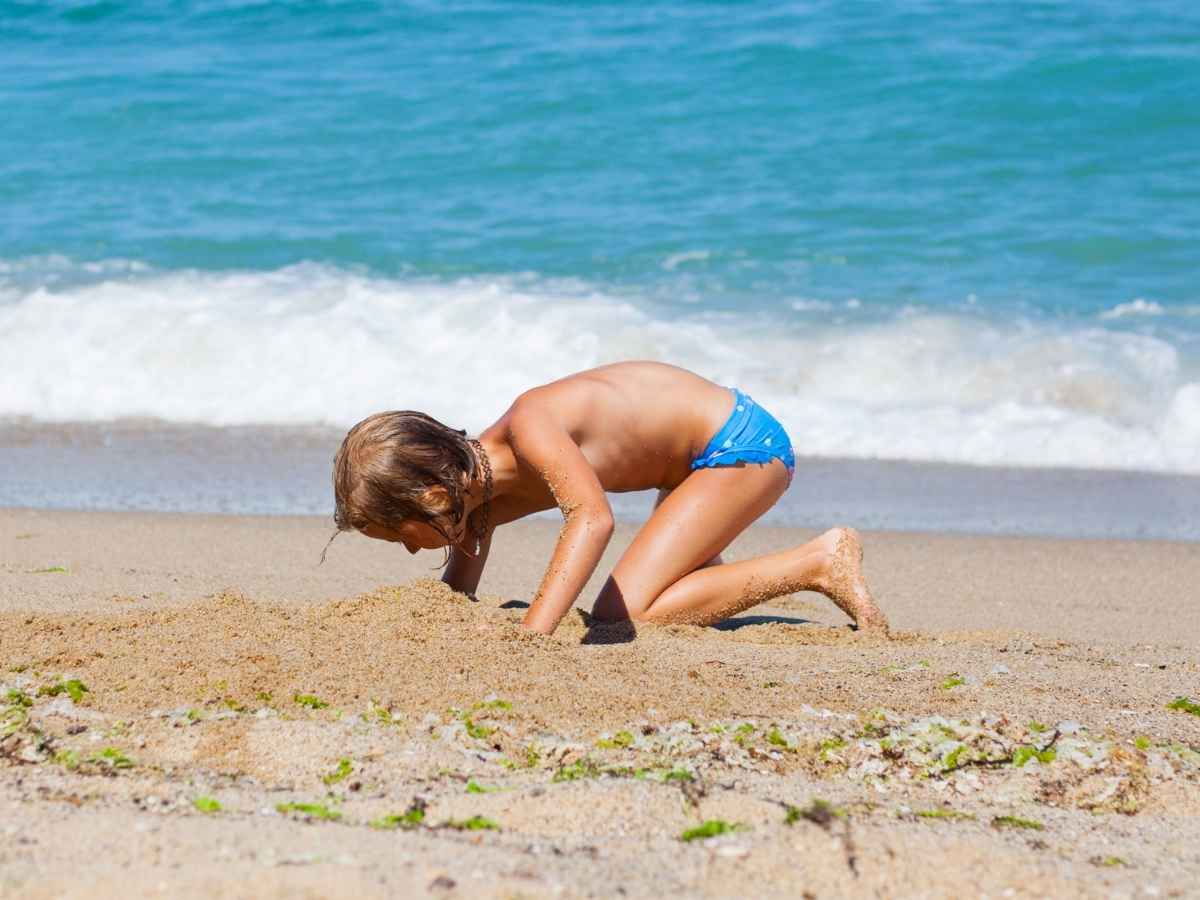 Bambino scava una buca in spiaggia al mare, i pericoli e i consigli