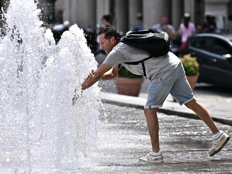 Una persona si rinfresca a una fontana in città