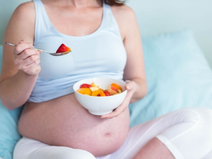 Una donna incinta mangia frutta seduta sul divano
