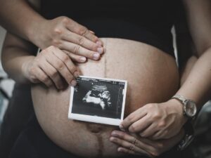 Una mamma e un padre si abbracciano e mostrano il pancione e l'ecografica del figlio