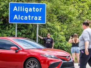 Il centro per migranti di Alligator Alcatraz, un uomo si fa scattare una foto sotto al cartello