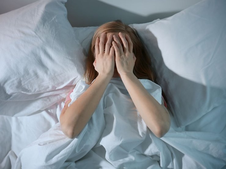 ragazza a letto con mani in faccia disperata