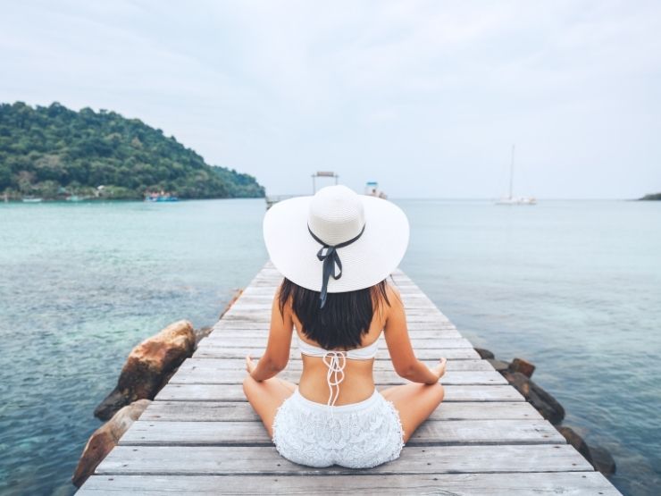 Una ragazza di spalle indossa un cappello e fa yoga al mare