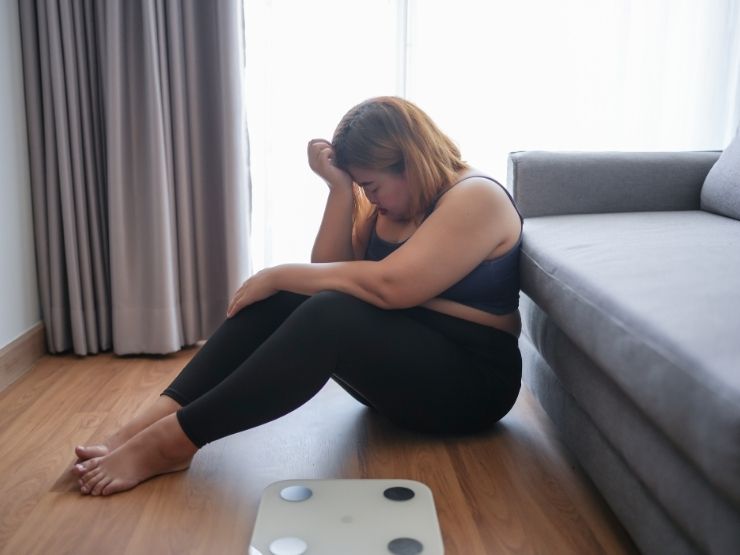 Una ragazza è triste a causa del suo peso ed è seduta sul pavimento