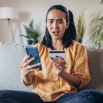 Una ragazza seduta sul divano al computer ha appena scoperto di essere stata truffata online