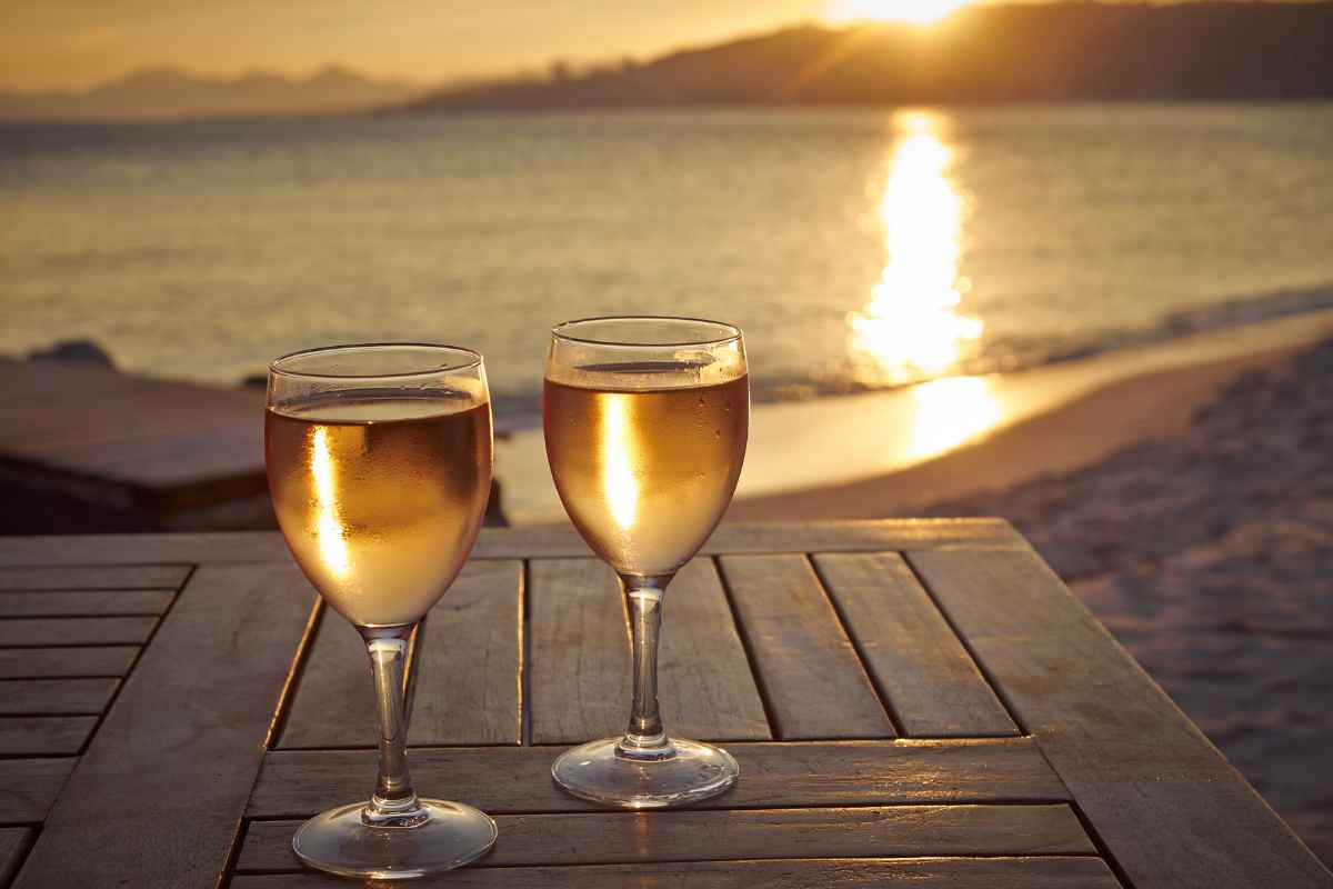 Calici di vino bianco su tavolo fronte mare al tramonto