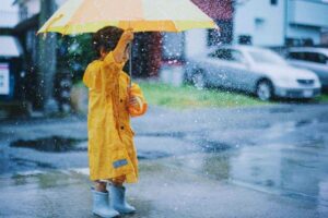 bambino sotto l'acqua con ombrello e impermeabile