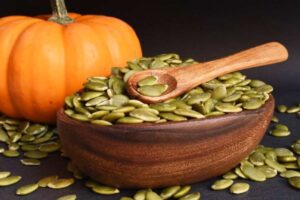 Semi di zucca verdi in una ciotola con una zucca sullo sfondo