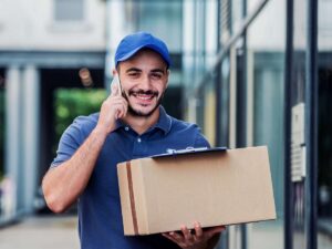 Un corriere consegna un pacco sorridente mentre parla al telefono col cliente.