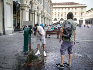 Un ragazzo di sciacqua la faccia sotto una fontanina per rinfrescarsi in estate in città