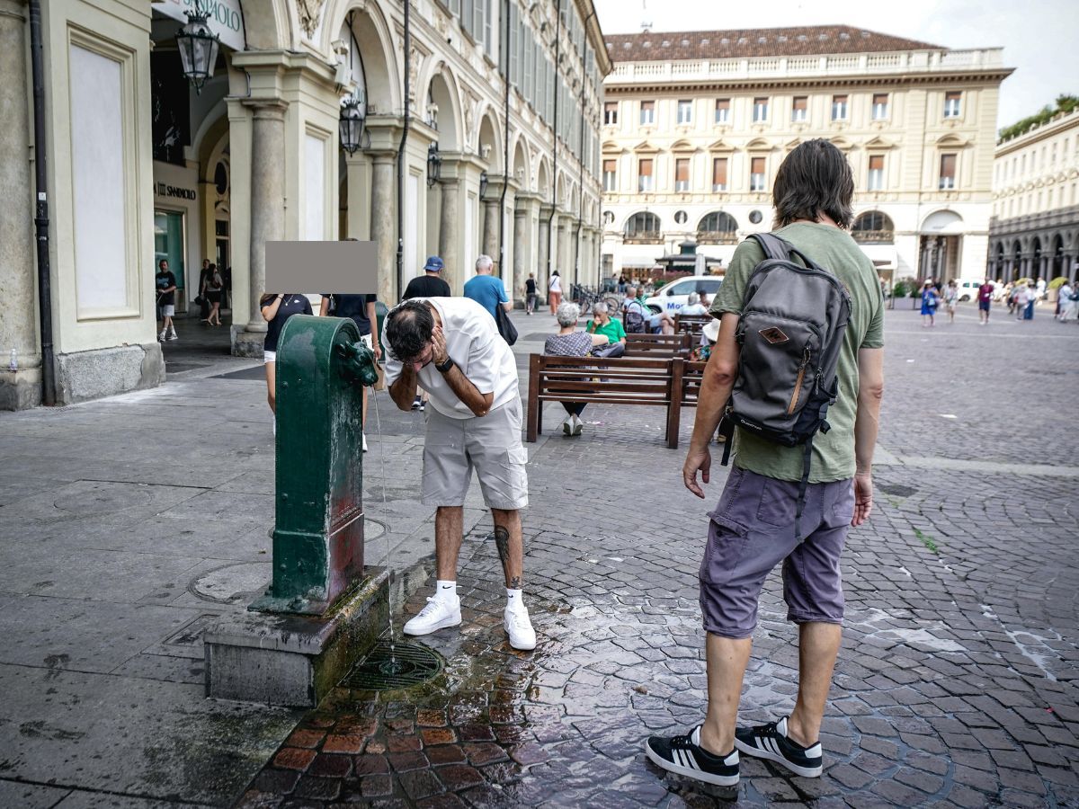 Un ragazzo di sciacqua la faccia sotto una fontanina per rinfrescarsi in estate in città